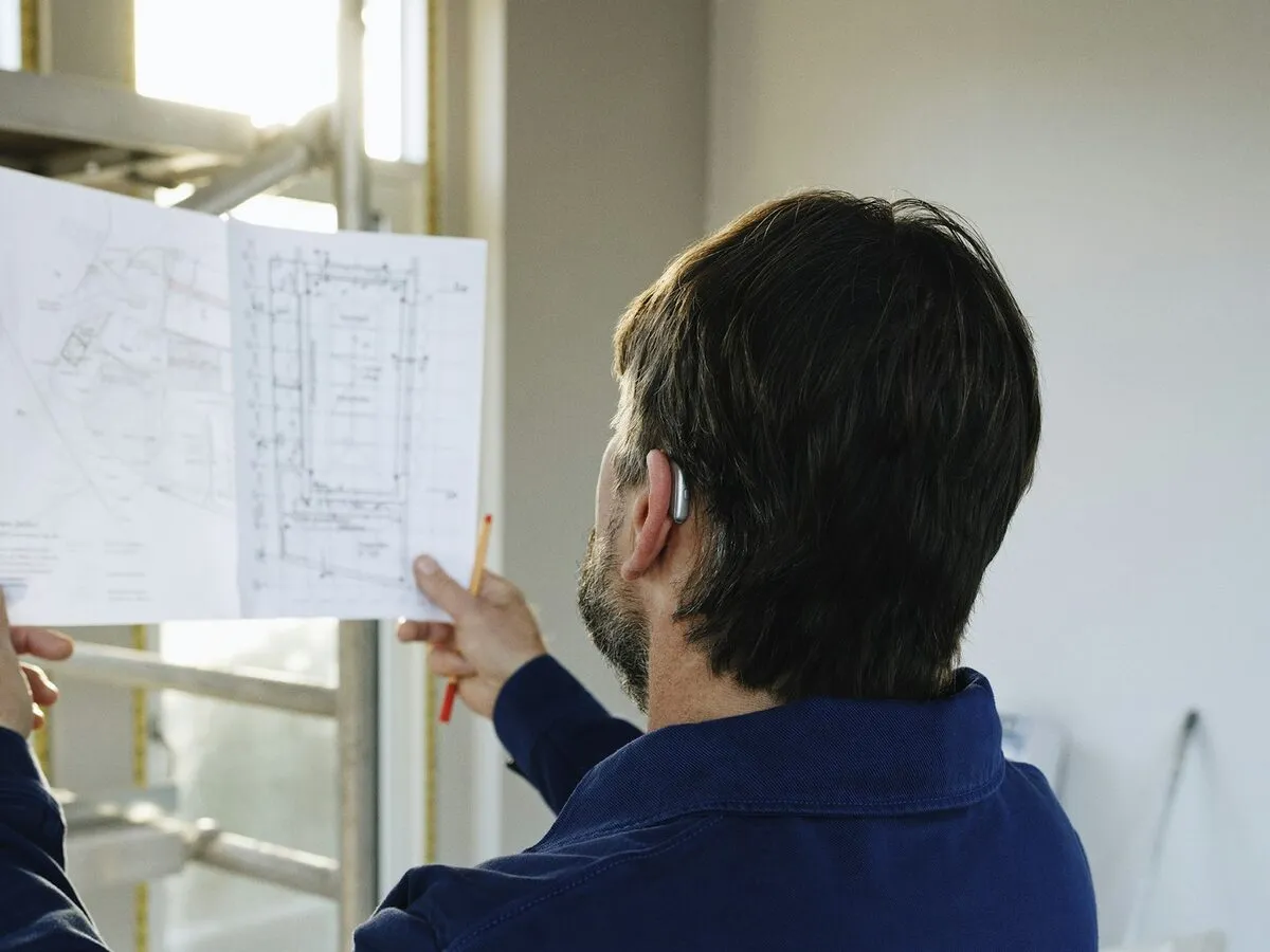 A contractor holding up building plans inside a house under renovation