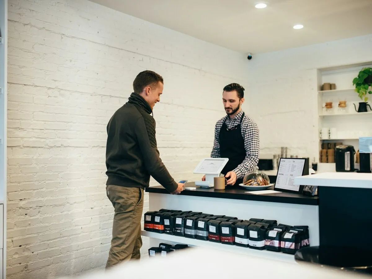 A shop owner in an apron helping a customer at the counter
