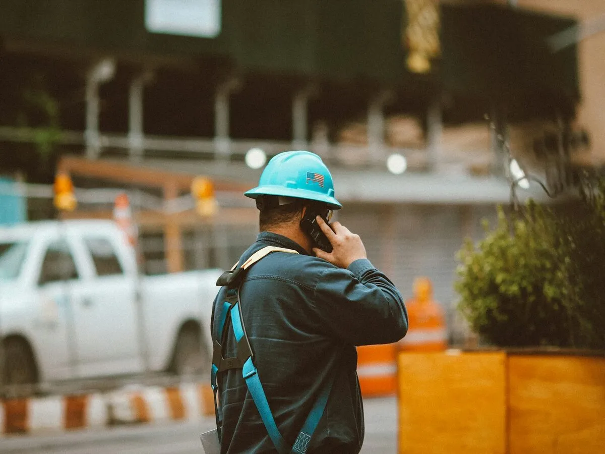 A worker in a hard hat and safety harness taking a call on a job site